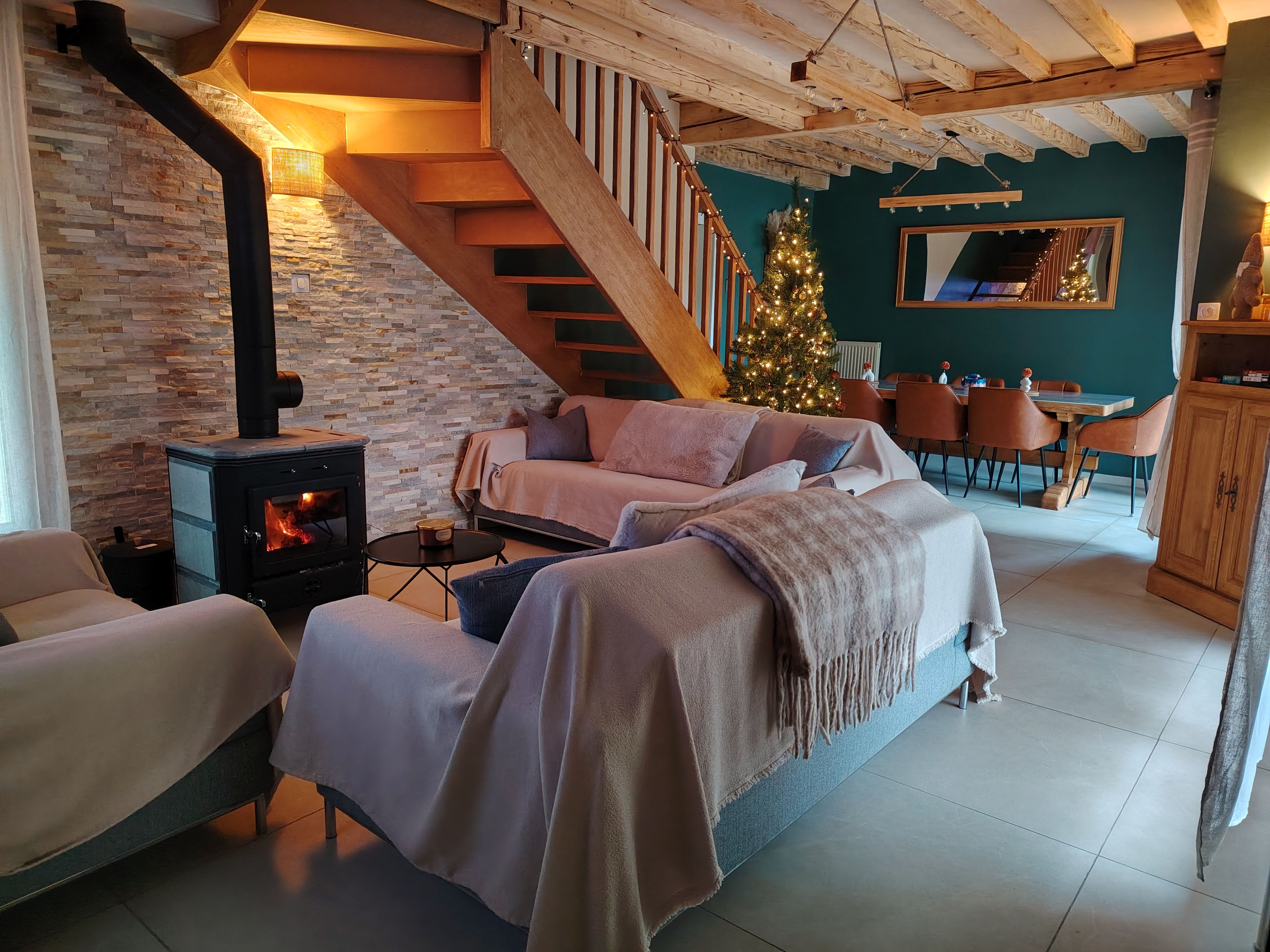 A cozy living room with a fireplace, a staircase, a Christmas tree, and a dining area.
