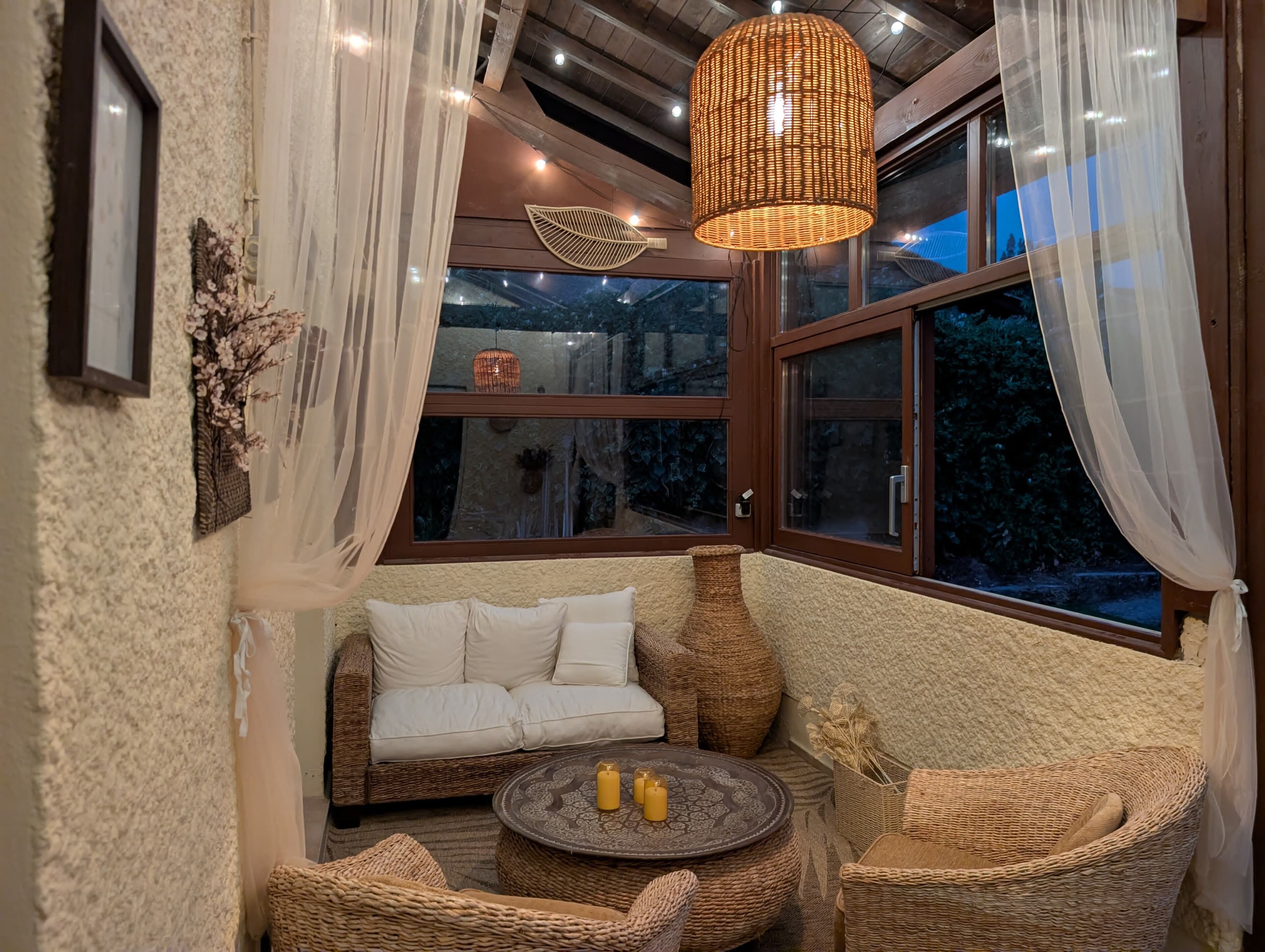Une pièce chaleureuse avec un coin salon confortable, une table ronde décorée de bougies et une grande fenêtre ornée de rideaux.