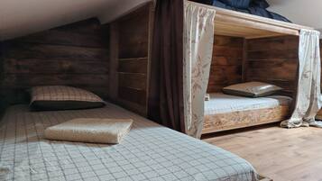 A room with two bunk beds, one with a canopy and wooden headboard, and the other with a plain headboard.