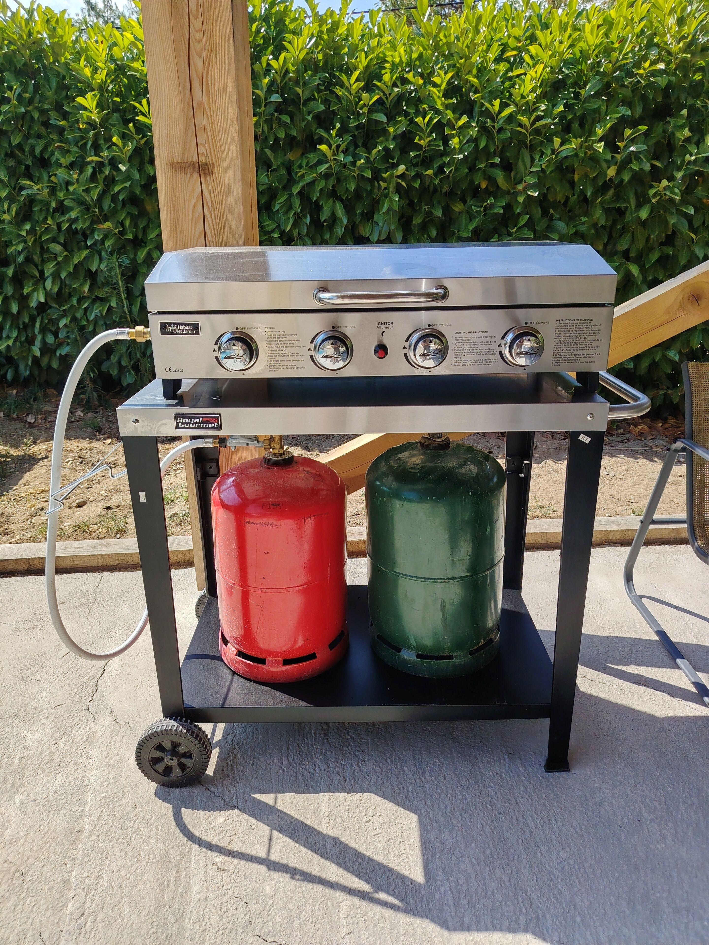 Een draagbare gasgrill met een bedieningspaneel, twee propaanflessen en een metalen frame.