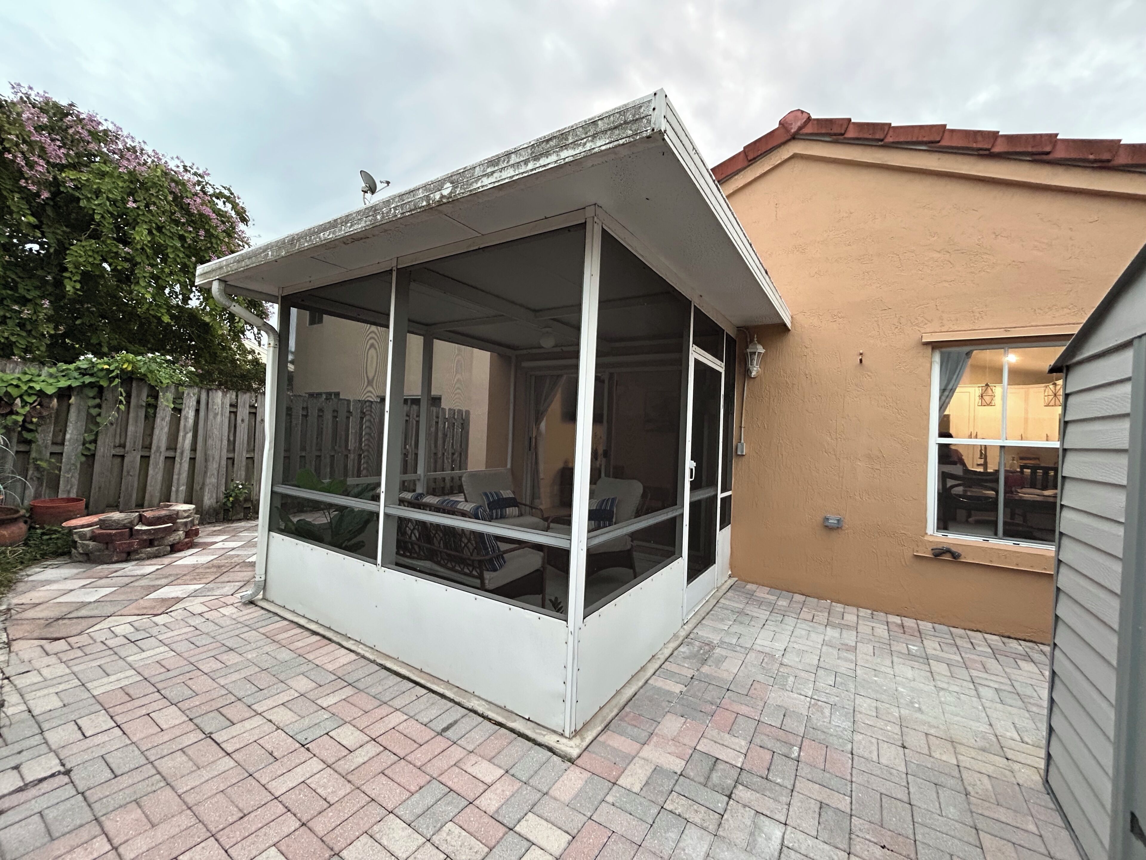 A covered patio area with a sliding glass door, a brick floor, and a wooden fence in the background.