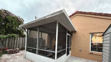 A covered patio area with a sliding glass door, a brick floor, and a wooden fence in the background.