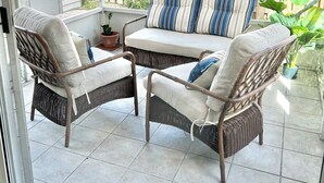 Eine überdachte Terrasse mit Korbmöbeln, einer gepolsterten Couch und Kübelpflanzen.