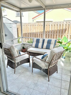 A covered patio with wicker furniture, a cushioned sofa, and potted plants. - Cozy 2-bedroom pet friendly family home in central Margate with pool access. (Margate)