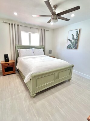 A bedroom with a bed, a nightstand, a ceiling fan, and a window with curtains. - Cozy 2-bedroom pet friendly family home in central Margate with pool access. (Margate)