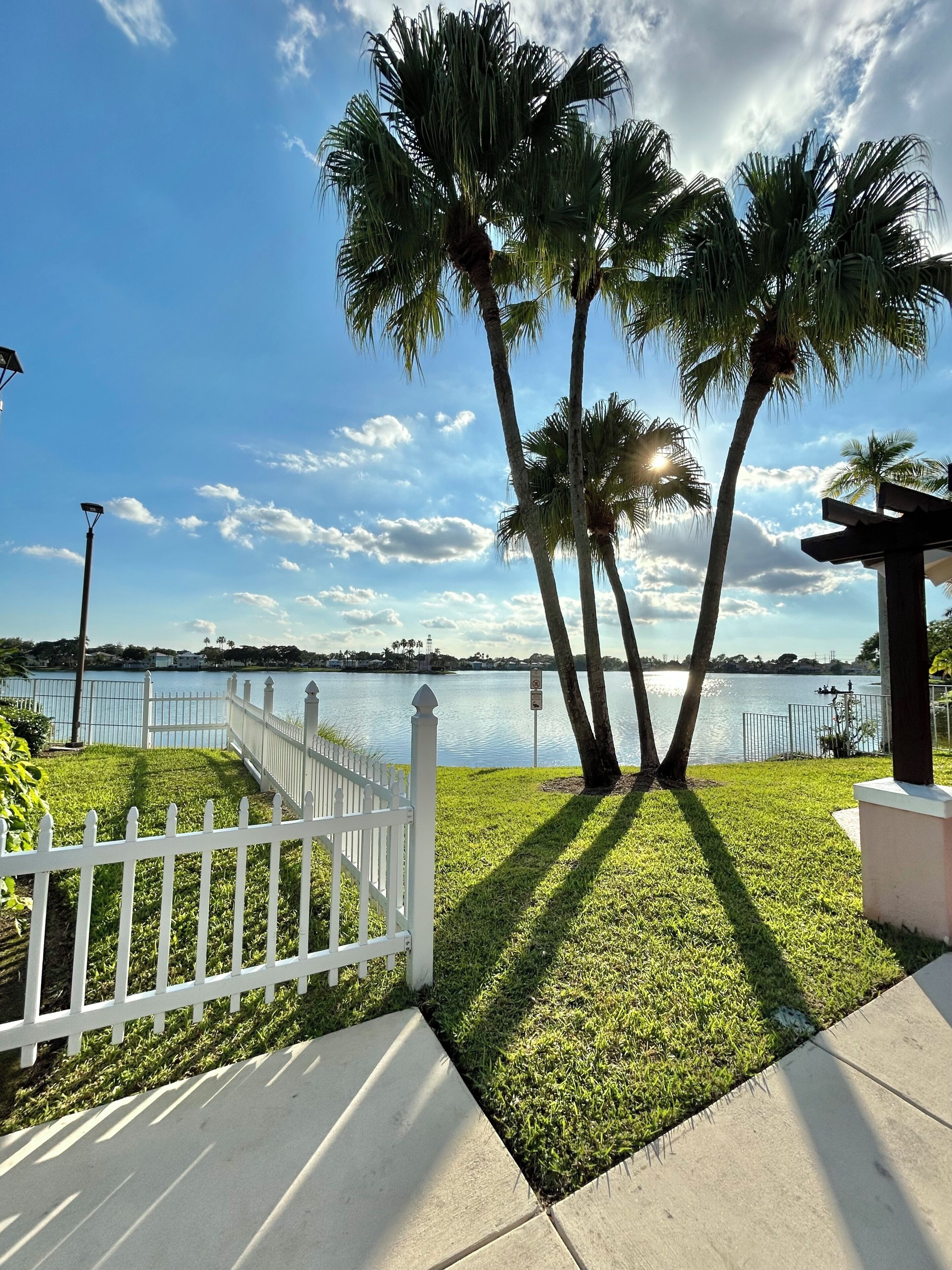 A waterfront property with a white fence, palm trees, and a clear sky.