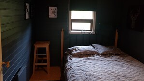 Un dormitorio con una cama individual, un taburete de madera, un ventanal con vistas y una pared decorada con un letrero que dice 'love'.