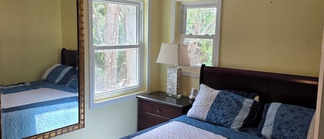 A bedroom with a bed, a ceiling fan, an air conditioning unit, and a window.