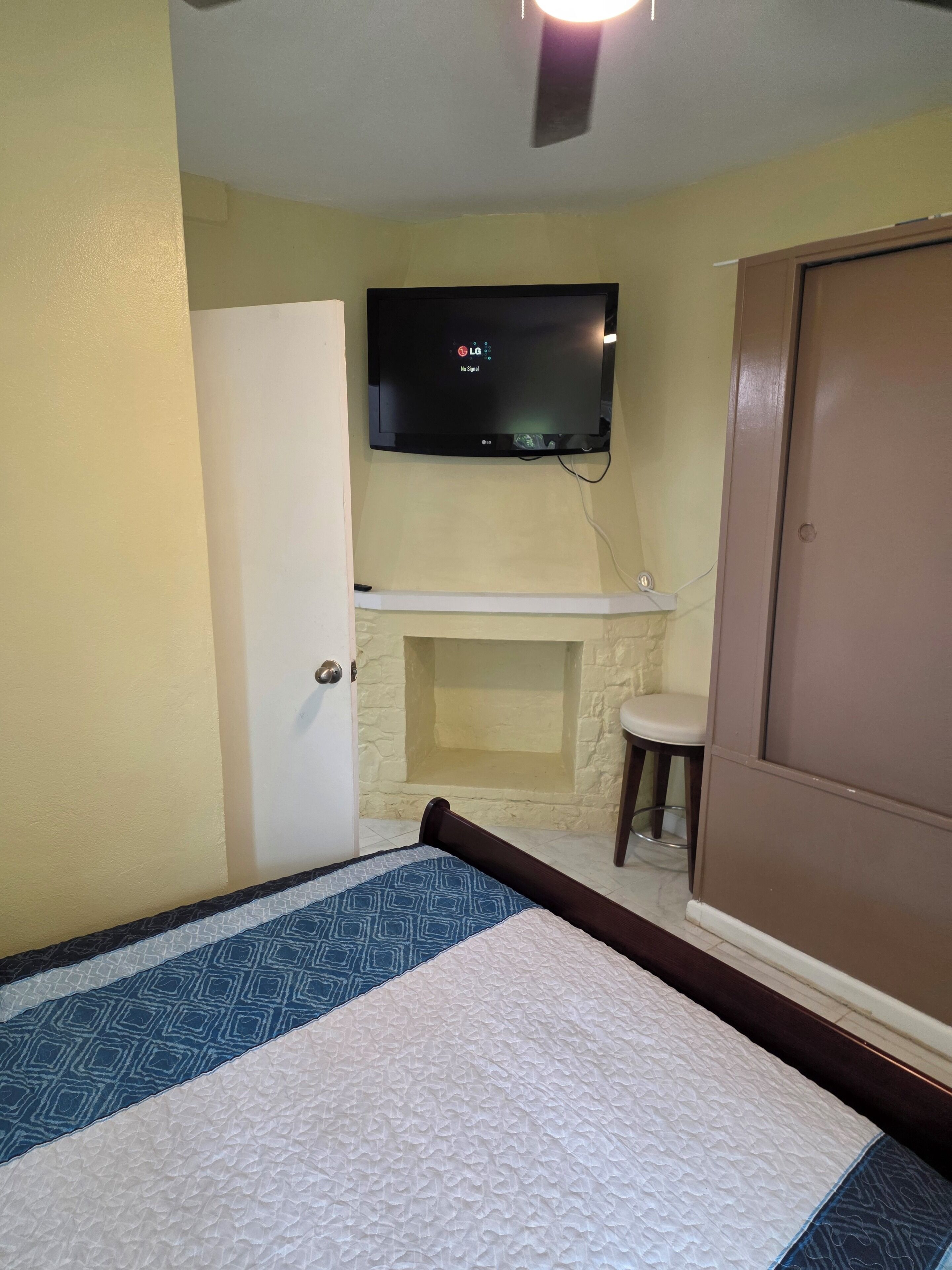Una habitación de hotel con una cama, televisor montado en la pared, una mesita y una puerta.