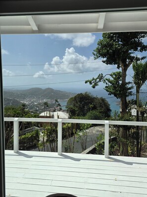 Blick von einem Balkon mit Geländer auf eine Küstenlandschaft mit Bergen und einem Gewässer.