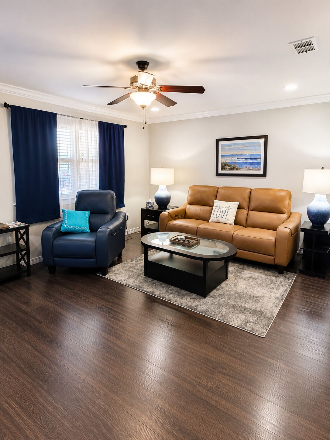 A living room with a ceiling fan, a sofa, a chair, a coffee table, and a painting on the wall.
