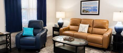A living room with a ceiling fan, a sofa, a chair, a coffee table, and a painting on the wall.