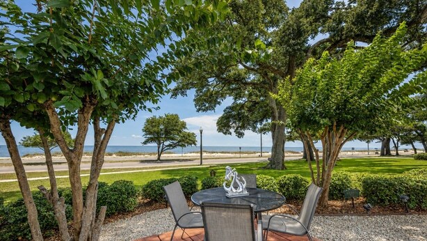 Un espace extérieur aménagé avec une table et des chaises, entouré d’arbres et offrant une vue sur la plage.