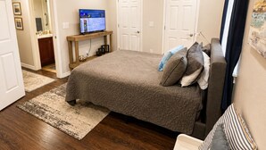 Une chambre à coucher avec un lit, un ventilateur de plafond, un téléviseur, et une salle de bain visible au fond.