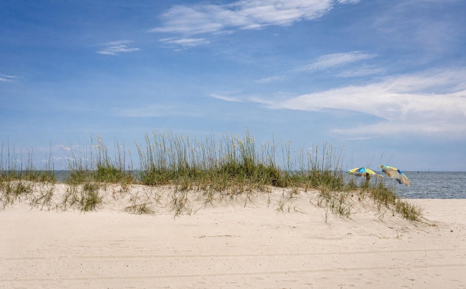 A beach with sand dunes and two beach umbrellas.