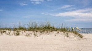 Une plage avec des dunes de sable et deux parasols.