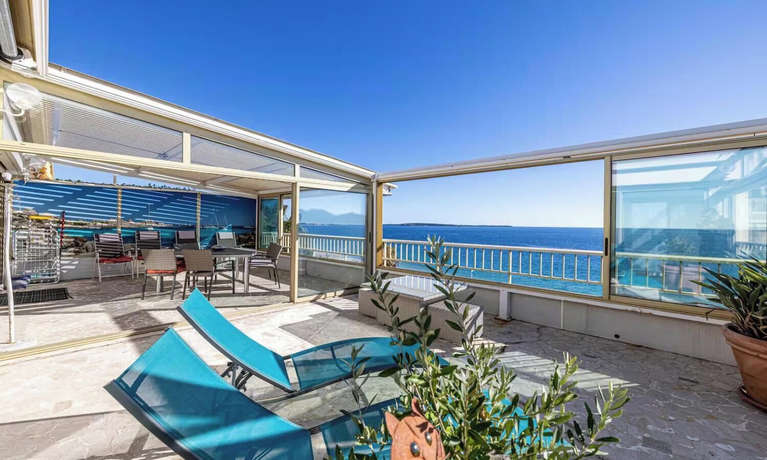 A sunlit outdoor deck with a pool, lounge chairs, and a view of the sea.