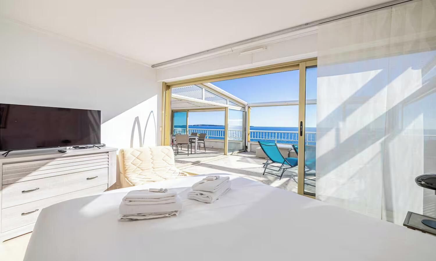A hotel room with a bed, a TV, a desk, and a balcony with a view of the sea.