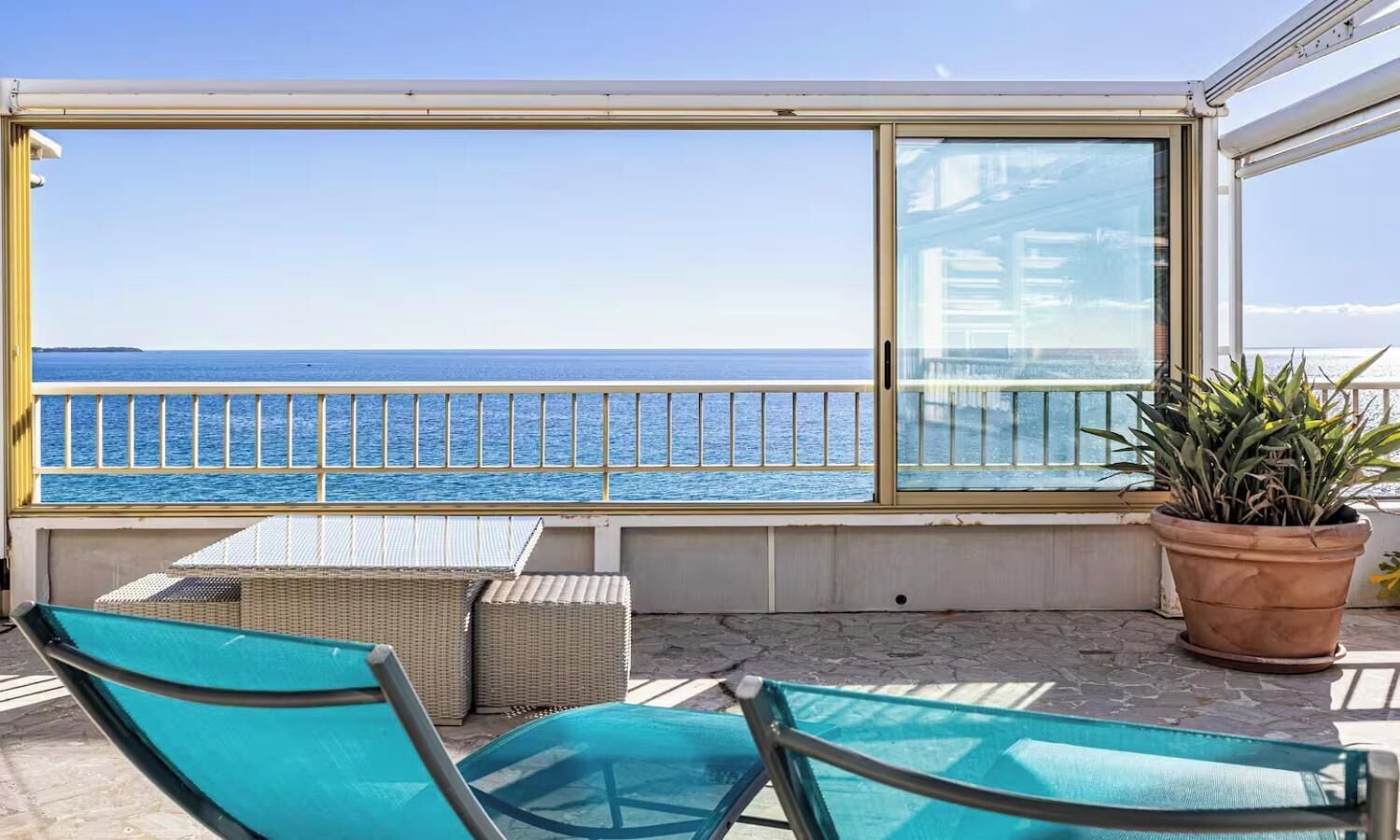 A balcony with a view of the sea, wicker furniture, and a potted plant.