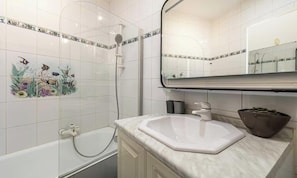 Ein Badezimmer mit weißem Waschbecken, einem Spiegel, einer Badewanne und dekorativen Fliesen.