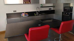 Cocina moderna con una isla central, dos taburetes rojos, horno empotrado y microondas.