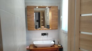 Baño con tocador de madera, lavamanos blanco, espejo y una pequeña cesta de mimbre.
