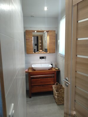 Ein Badezimmer mit einem Holzwaschtisch, einer weißen Spüle, einem Spiegel und einem kleinen Korbwäschesammler.