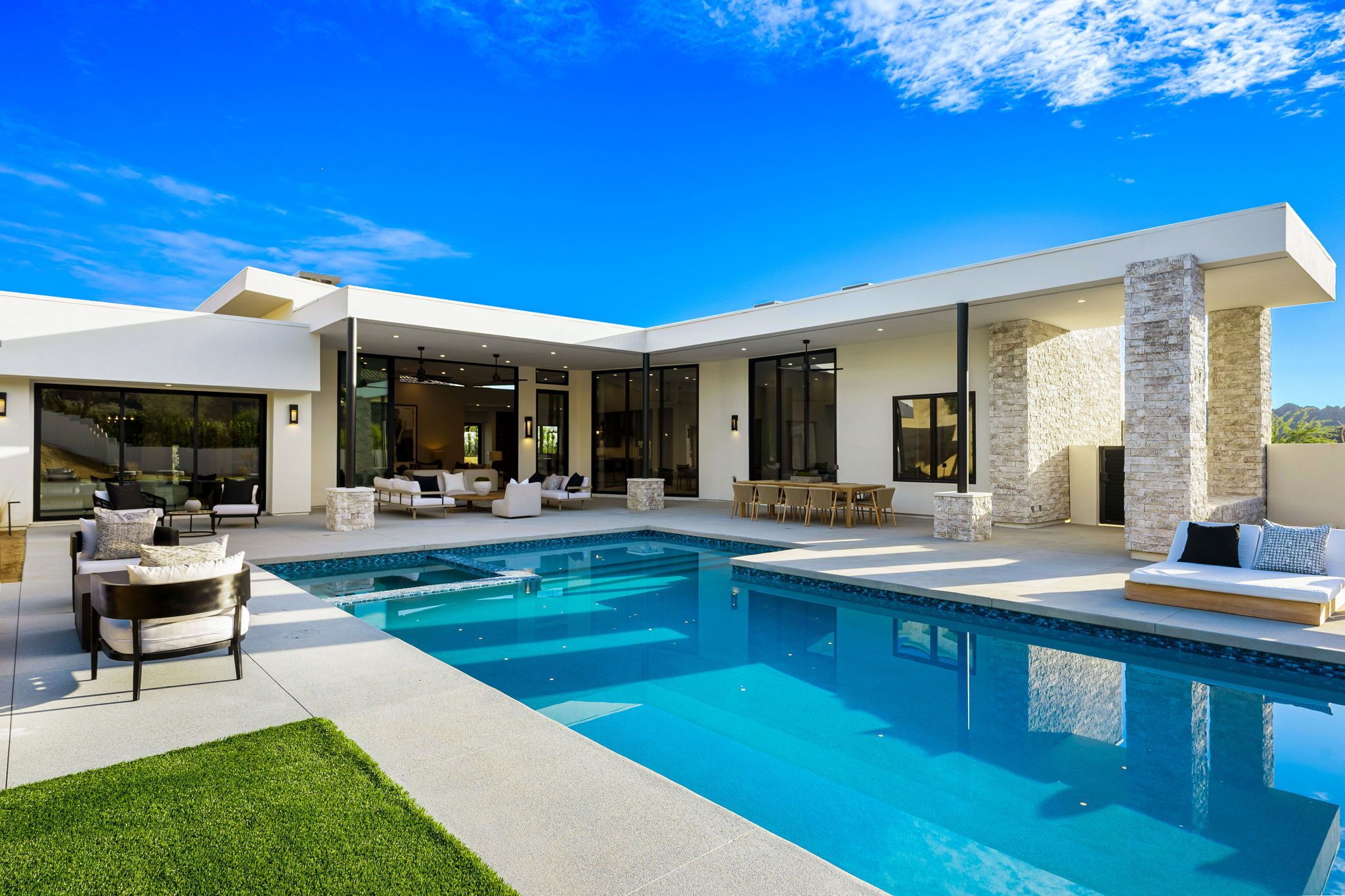 Ein modernes Haus mit Swimmingpool, Sitzgelegenheiten im Freien und großen Fenstern.