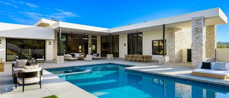 Une maison moderne dotée d’une piscine, d’un espace salon extérieur et de grandes fenêtres.