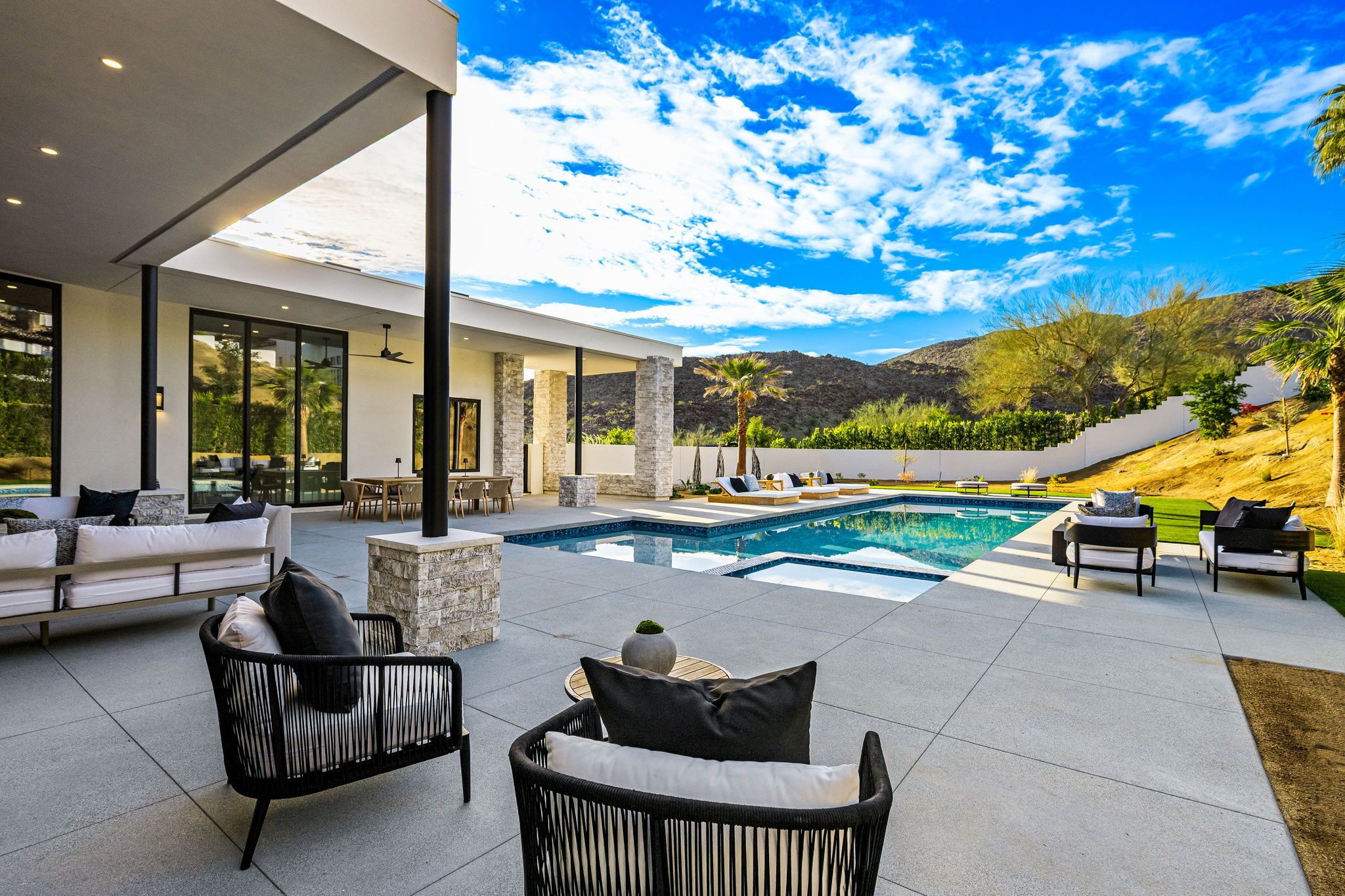 Ein moderner Poolbereich im Freien mit Liegestühlen, einem Essplatz und Blick auf eine gebirgige Landschaft.