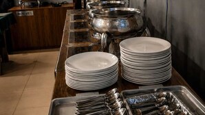 A buffet setup with stacked plates and serving utensils, a non-vegetarian sign, and a window with blinds. - sennin evin & resorts by MH (Srinagar)