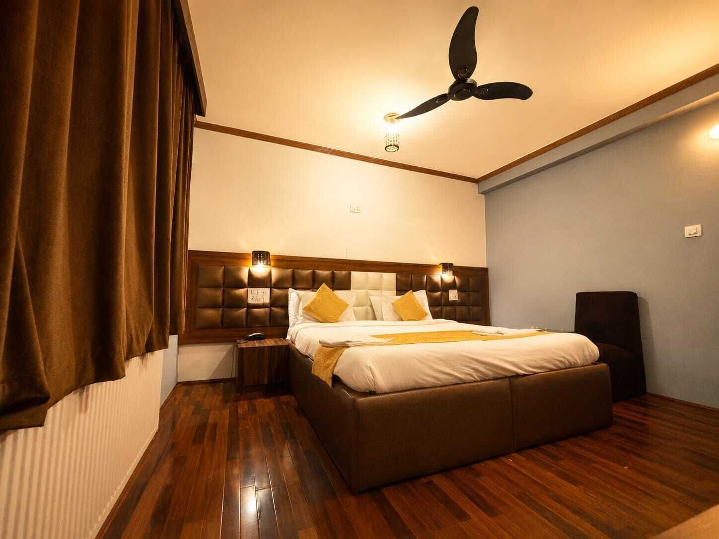 Una habitación de hotel con una cama grande, un ventilador de techo y una mesita de noche con lámpara.