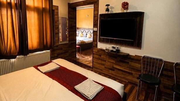 Habitación de hotel con una cama, un televisor de pantalla plana en la pared, un ventilador de techo y suelo de madera.