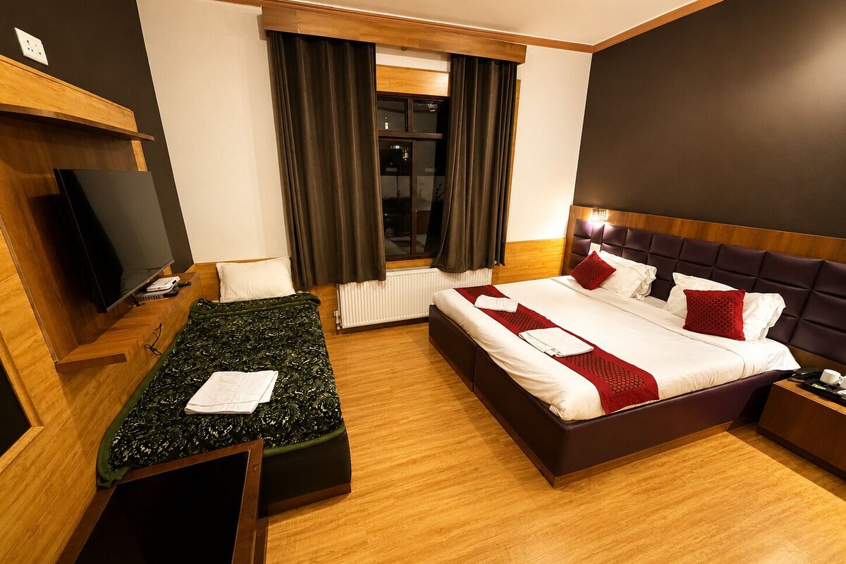 Una habitación de hotel con cama, escritorio, televisor y ventana con cortinas.