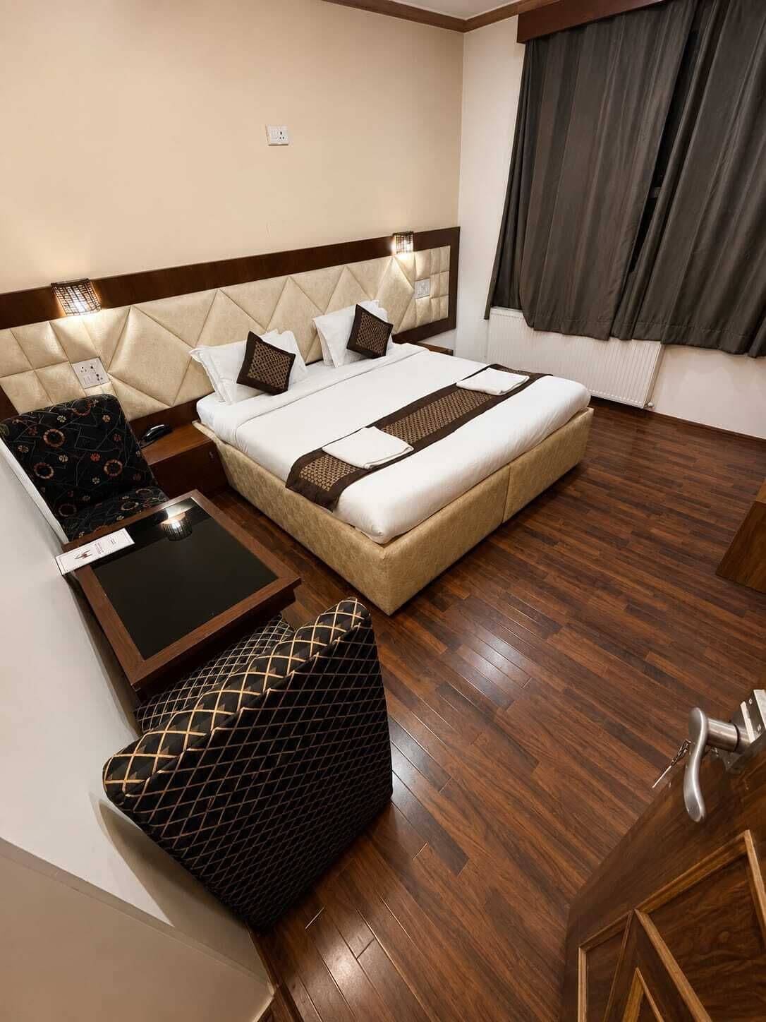 A hotel room with a large bed, a bedside table, a chair, and a wooden floor.