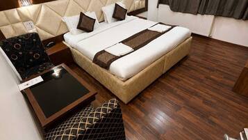 A hotel room with a large bed, a bedside table, a chair, and a wooden floor.