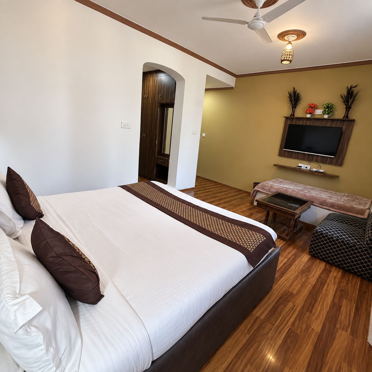 Quarto com cama grande, TV na parede e ventoinha no teto.