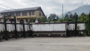 Un amplio espacio al aire libre con suelo pavimentado, una pared de ladrillo blanco con macetas verdes y un edificio con techo inclinado al fondo.