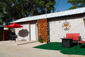 Ein möblierter Patio-Bereich im Freien mit Grill, rotem Sonnenschirm und Sitzgelegenheiten.