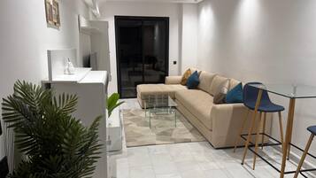 Una sala moderna con un sofá, una mesa de centro de vidrio y una mesita auxiliar.