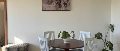 A dining area with a round table, white chairs, a potted plant, and a framed picture on the wall.