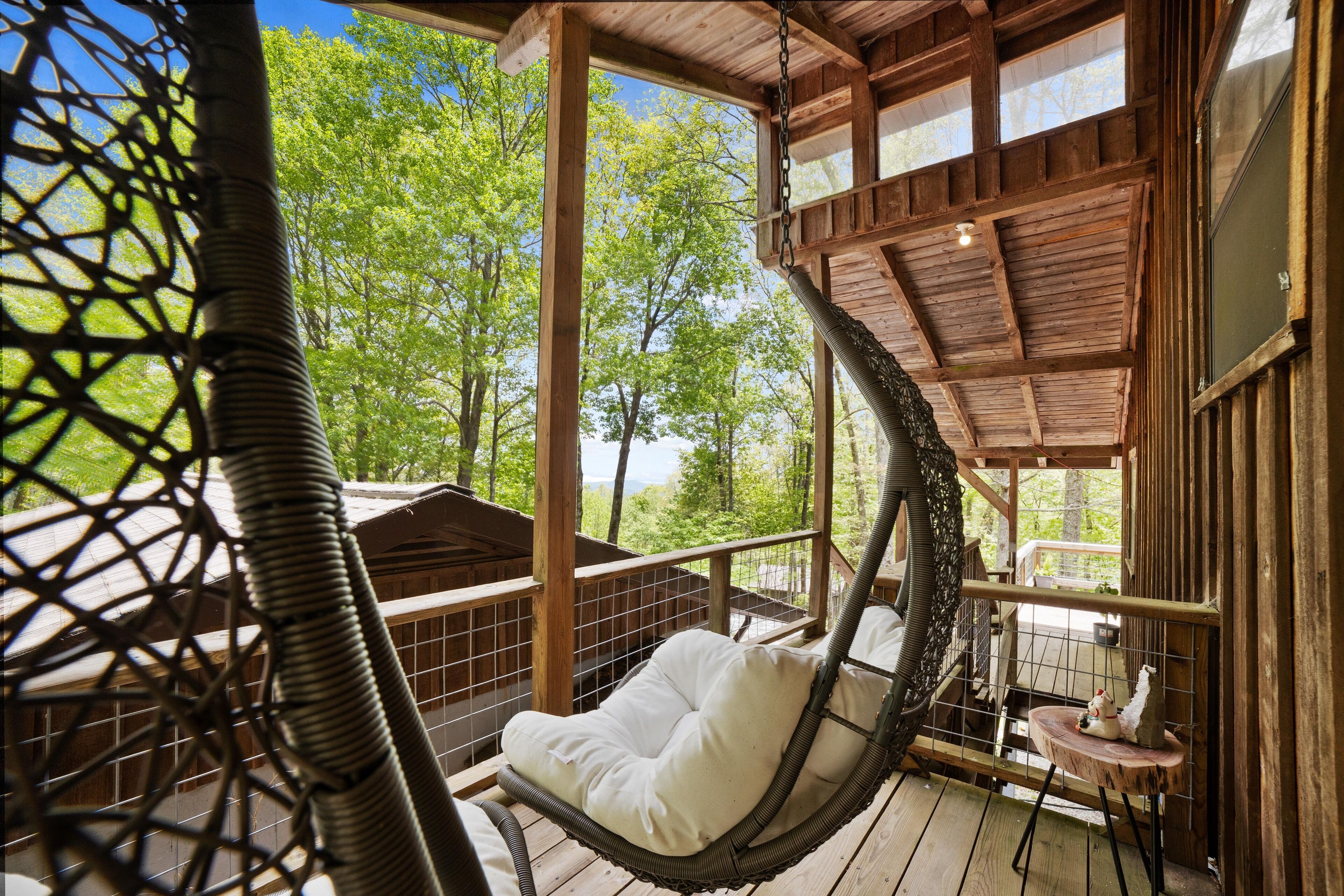 Une terrasse en bois avec un fauteuil suspendu et une petite table agrémentée d’un objet décoratif.