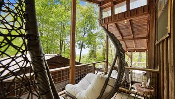Une terrasse en bois avec un fauteuil suspendu et une petite table agrémentée d’un objet décoratif.