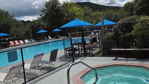 A swimming pool area with lounge chairs and umbrellas, surrounded by a fence. - Cozy 1-bedroom apartment in charming Sky Valley, GA. 11 miles from Highlands, NC (Dillard)
