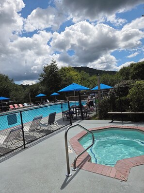 A swimming pool area with lounge chairs and umbrellas, surrounded by a fence.