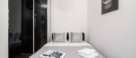 A modern bedroom with a bed, pillows, a magazine, and a towel.
