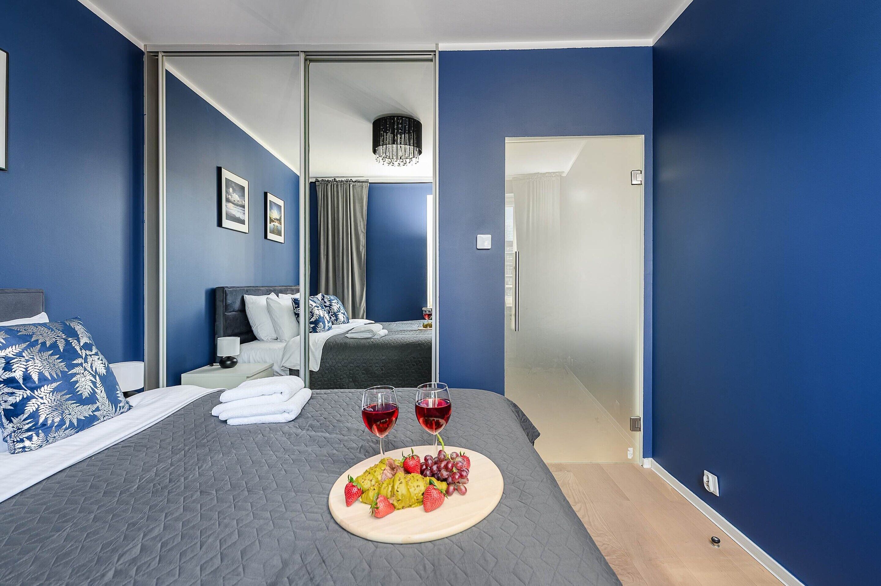 Een hotelkamer met een bed, een nachtkastje met een lamp, een muur met ingelijste foto's en een deur naar een andere kamer.
