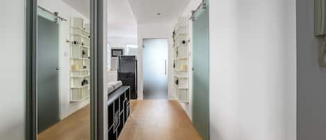 A hallway with a kitchen area, wooden flooring, and built-in shelving units.