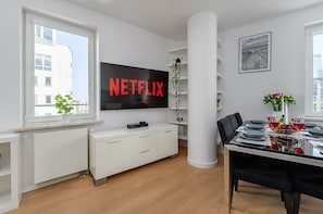 A modern living room with a flat-screen TV mounted on the wall, a dining table with chairs, and a potted plant. - Central Warsaw Home With Garage (Warsaw)