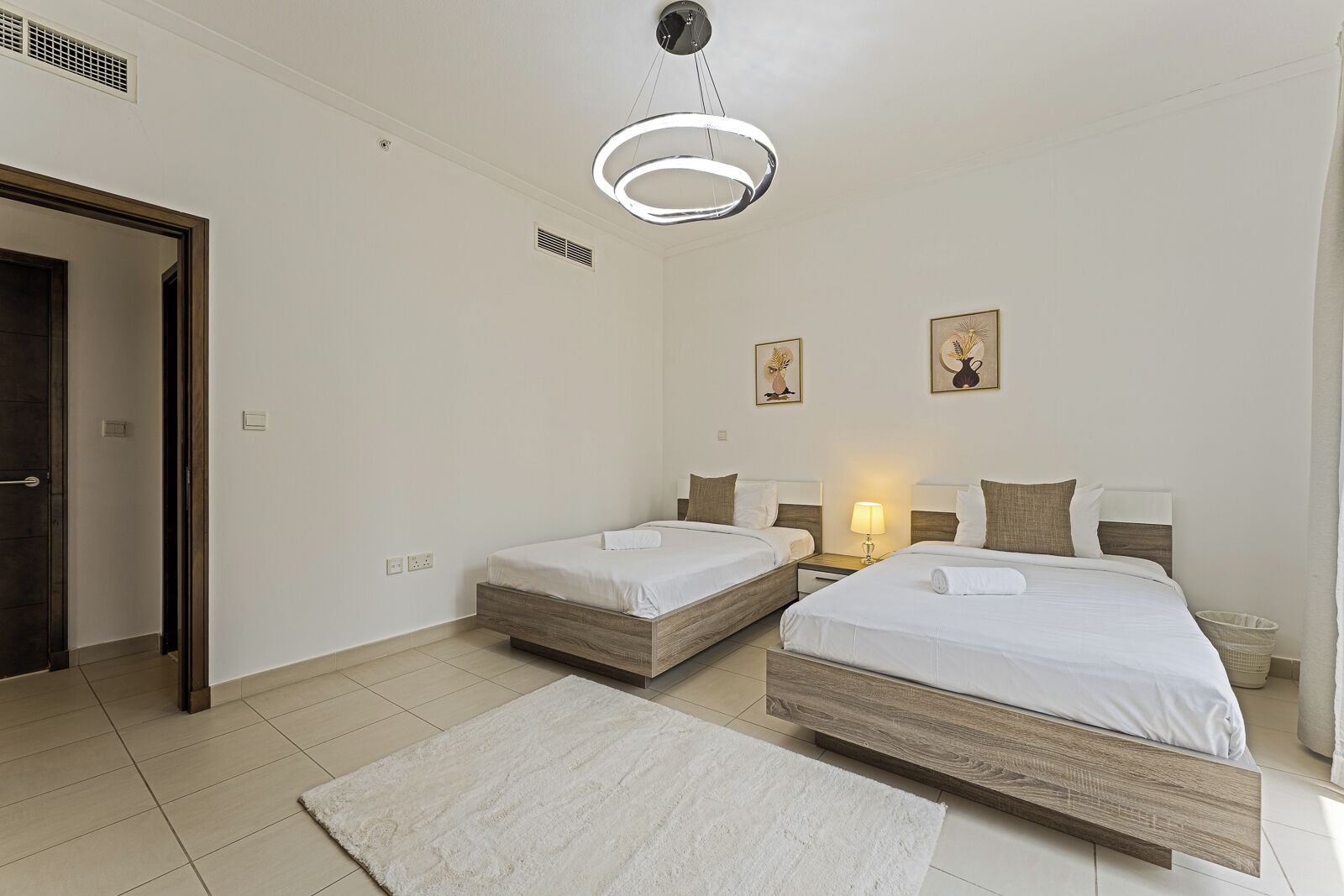 Een hotelkamer met twee eenpersoonsbedden, een grote spiegel, een plafondlamp en een klein nachtkastje met een lamp.
